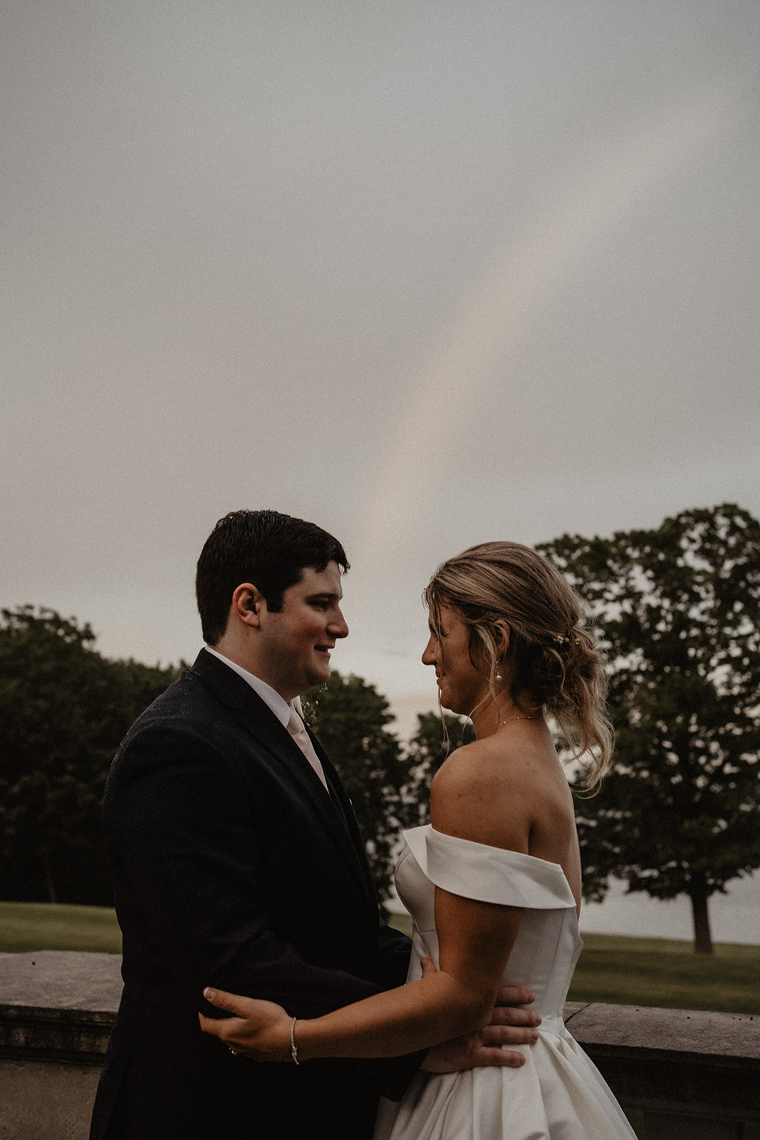 bride and groom looking at each other with rainbow in the background