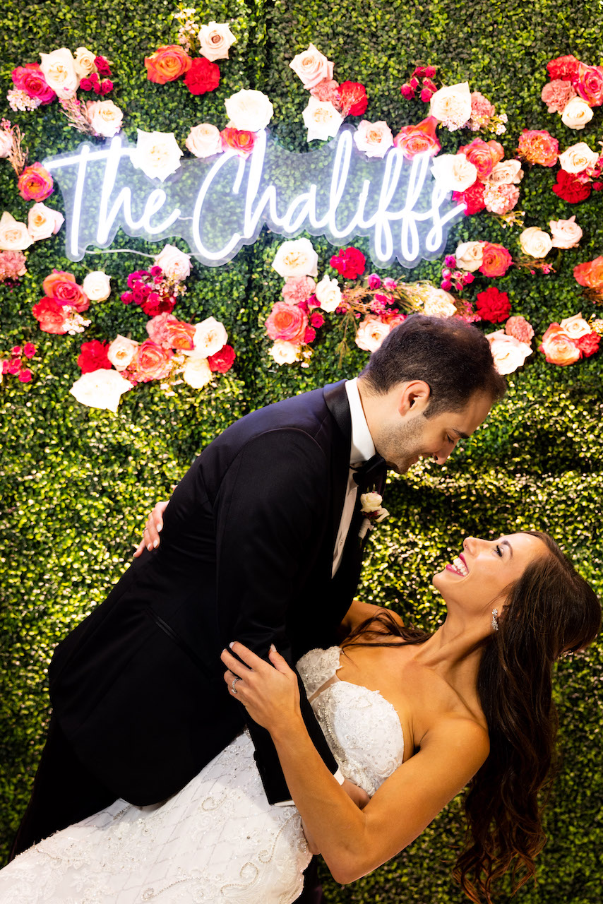 groom and bride in front of neon sign 