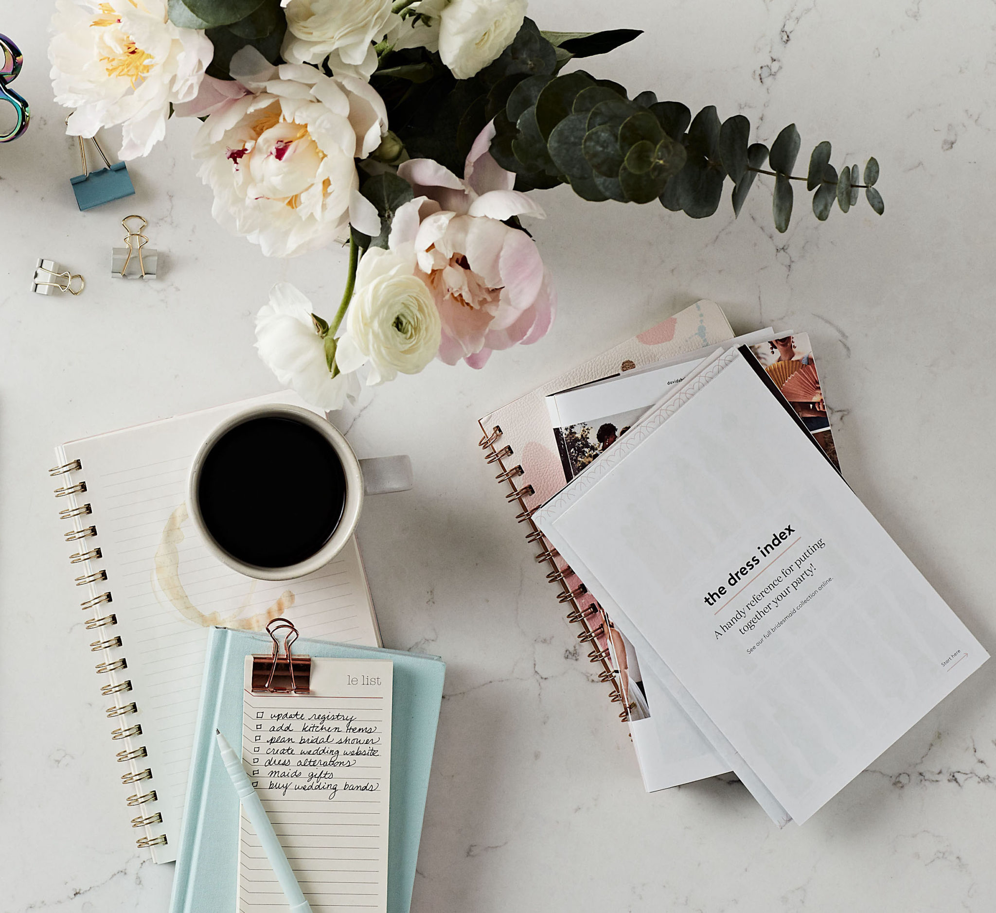 flatlay of wedding planning with notebook, flowers, and coffee