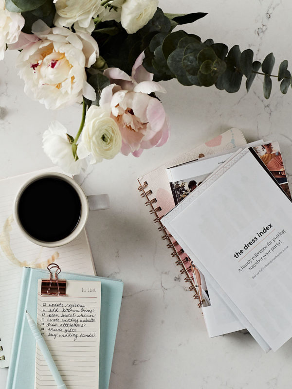 flatlay of wedding planning with notebook, flowers, and coffee