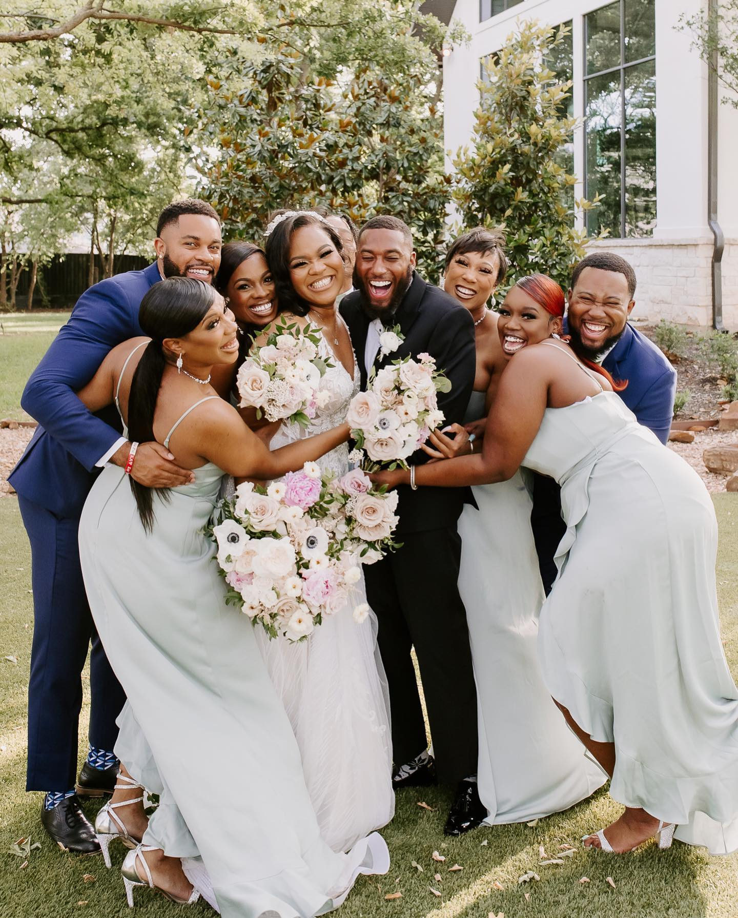 bridal party in blue bridesmaid dresses hug bride and groom