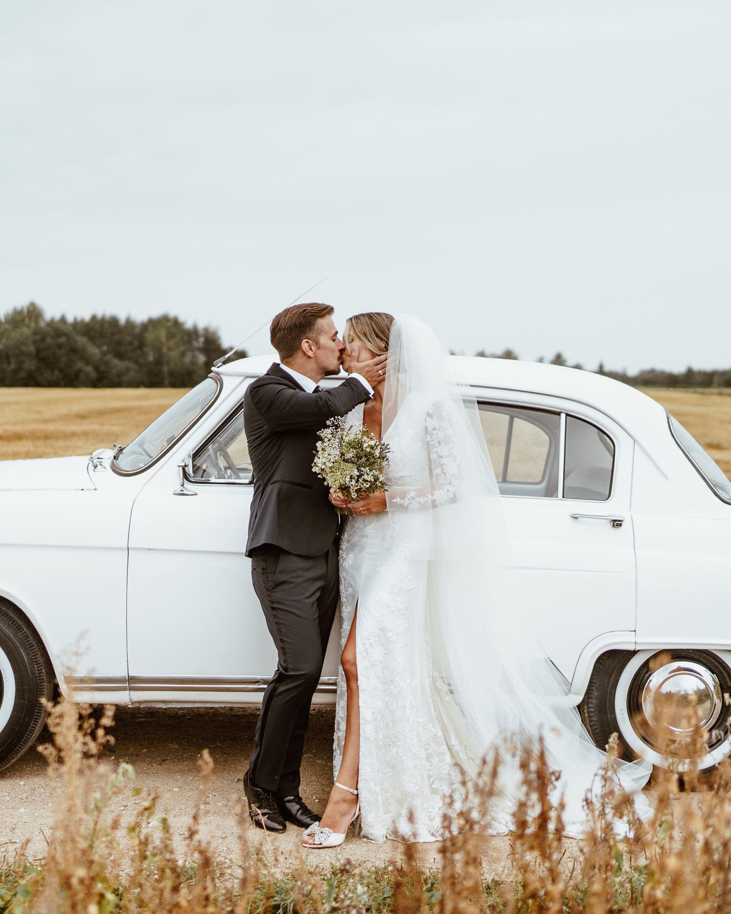 bride and groom in field with vintage getaway car